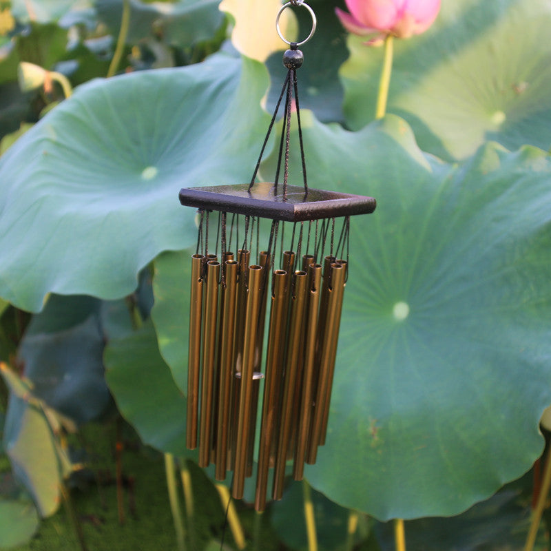 Bronze wind chime hanging among large green leaves
