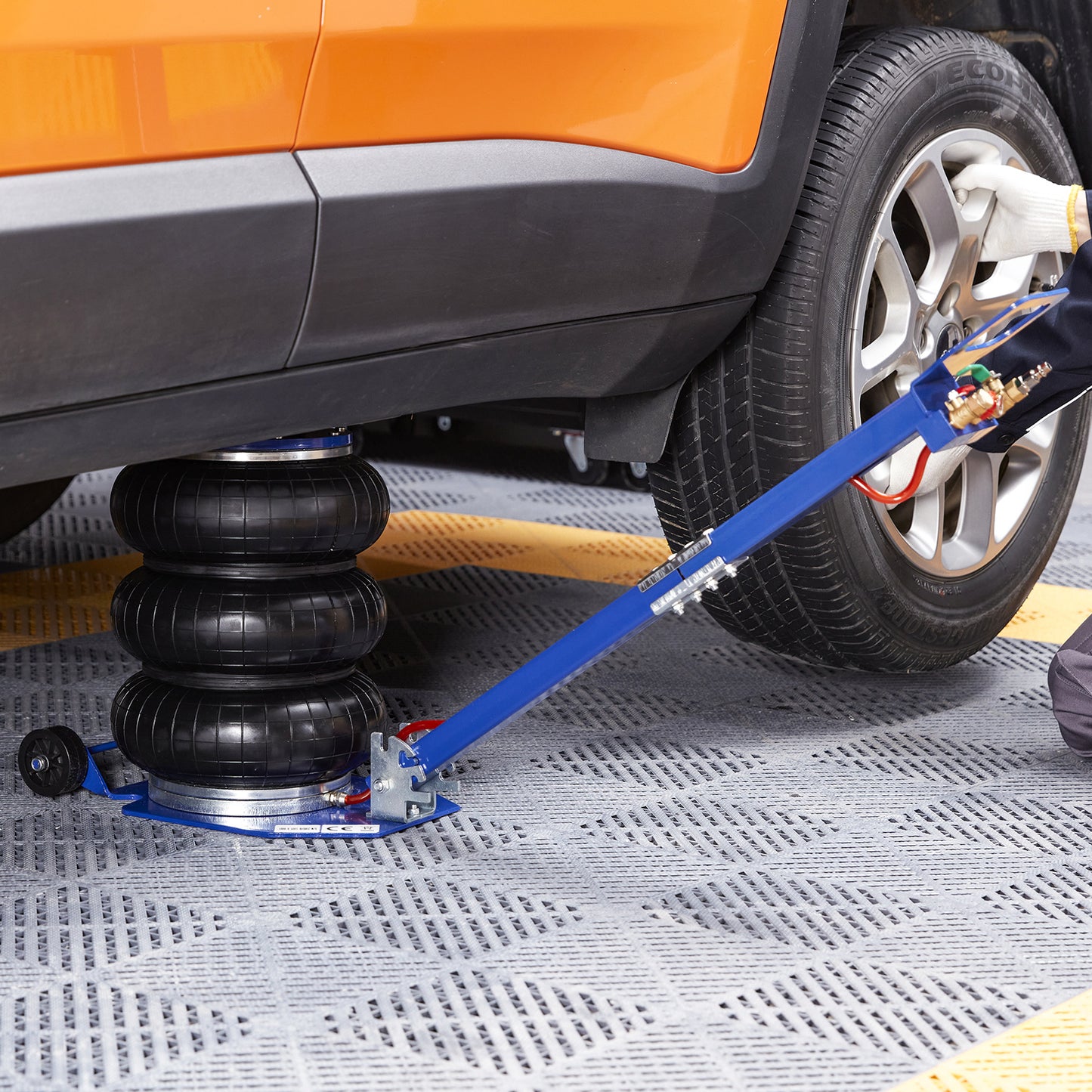 Car jack lifting a car with an orange fender on a textured surface