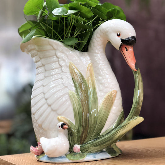 Ceramic swan planter with a small duck and greenery on a wooden surface.