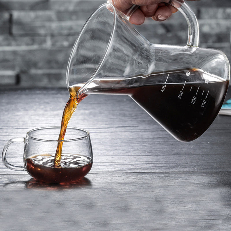 Glass carafe pouring coffee into a glass mug on a wooden surface.