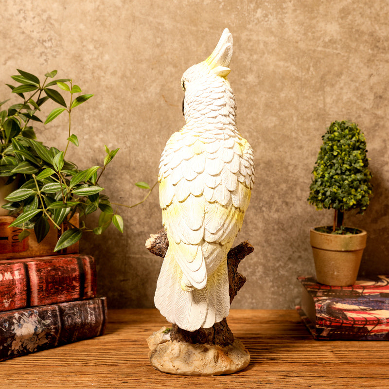 Decorative parrot statue on a wooden surface with plants and books in the background