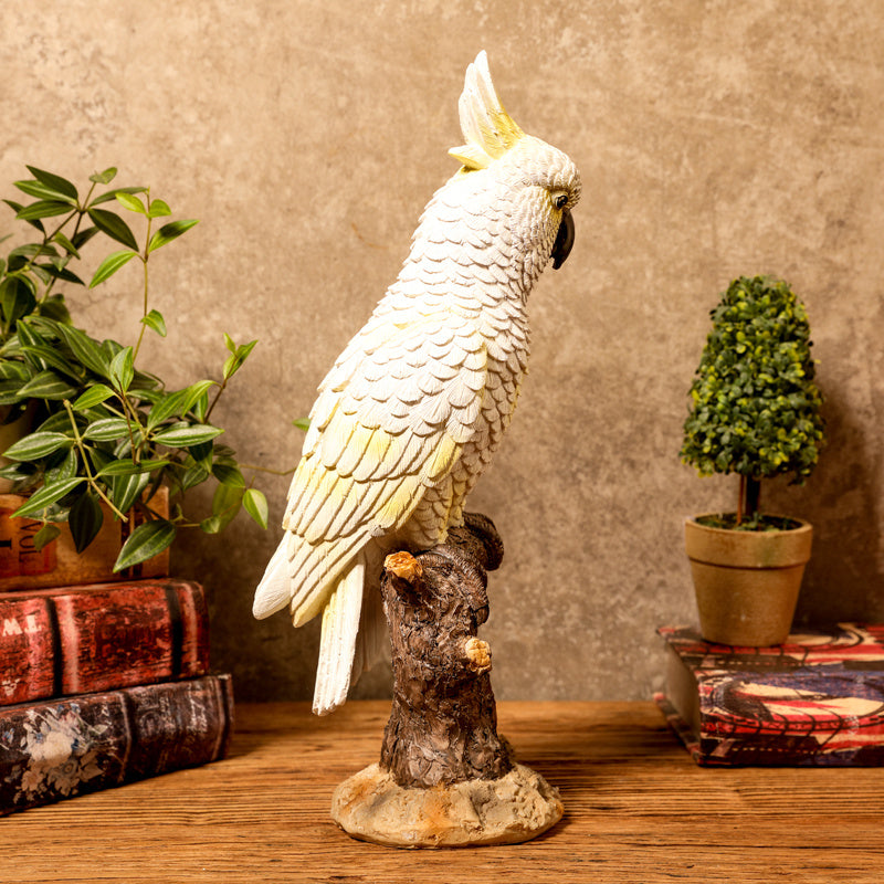 Decorative parrot statue on a wooden surface with plants and books in the background