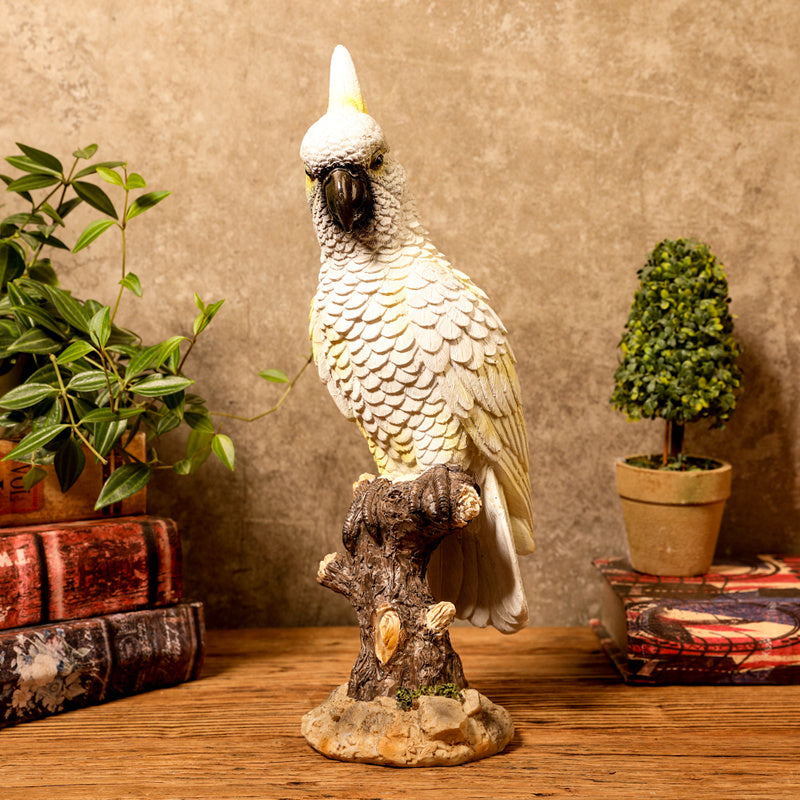 Decorative parrot statue on a wooden surface with plants and books in the background