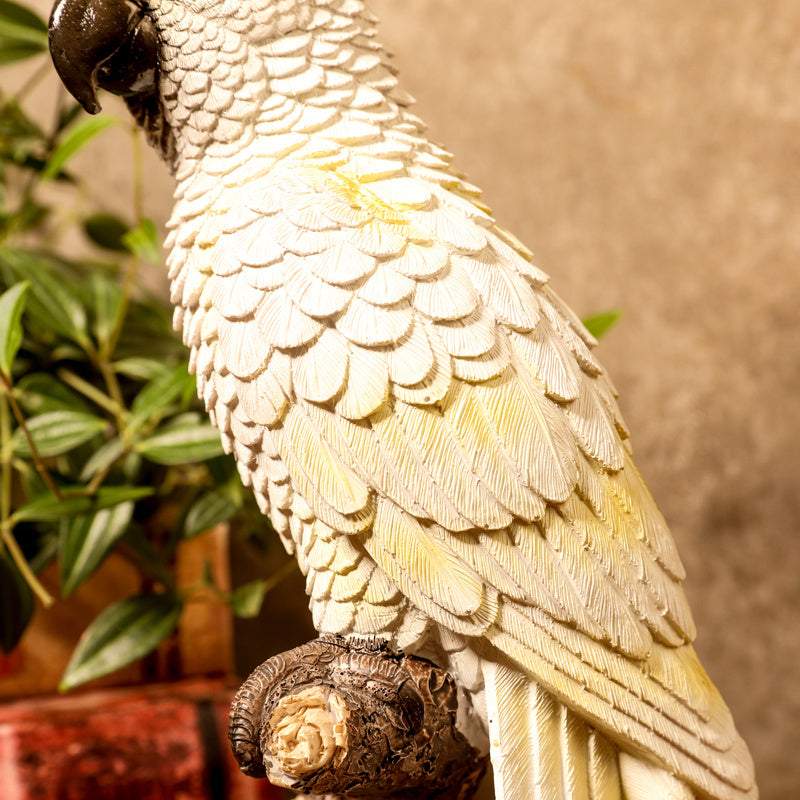 Close-up of a parrot statue with a blurred plant and wall in the background