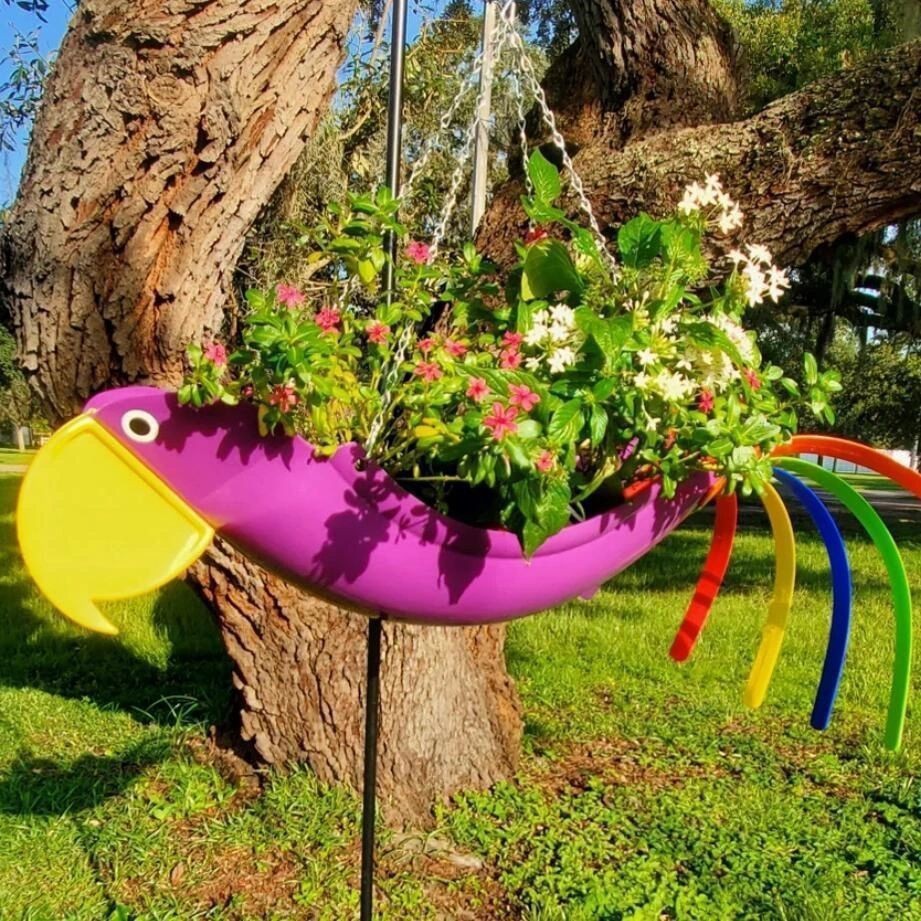Colorful parrot-shaped planter hanging from a tree with flowers.