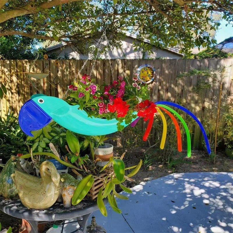 Colorful garden decoration with a blue snake-like object, flowers, and a bird on a table outdoors.