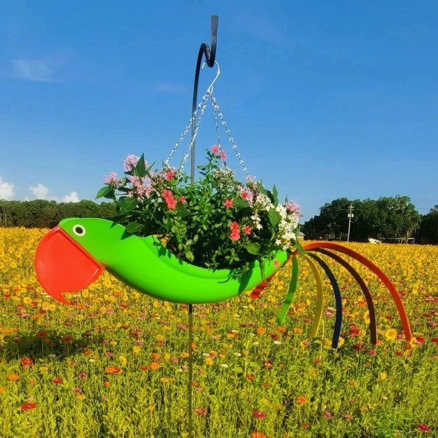Colorful bird-shaped planter with flowers against a blue sky and field background