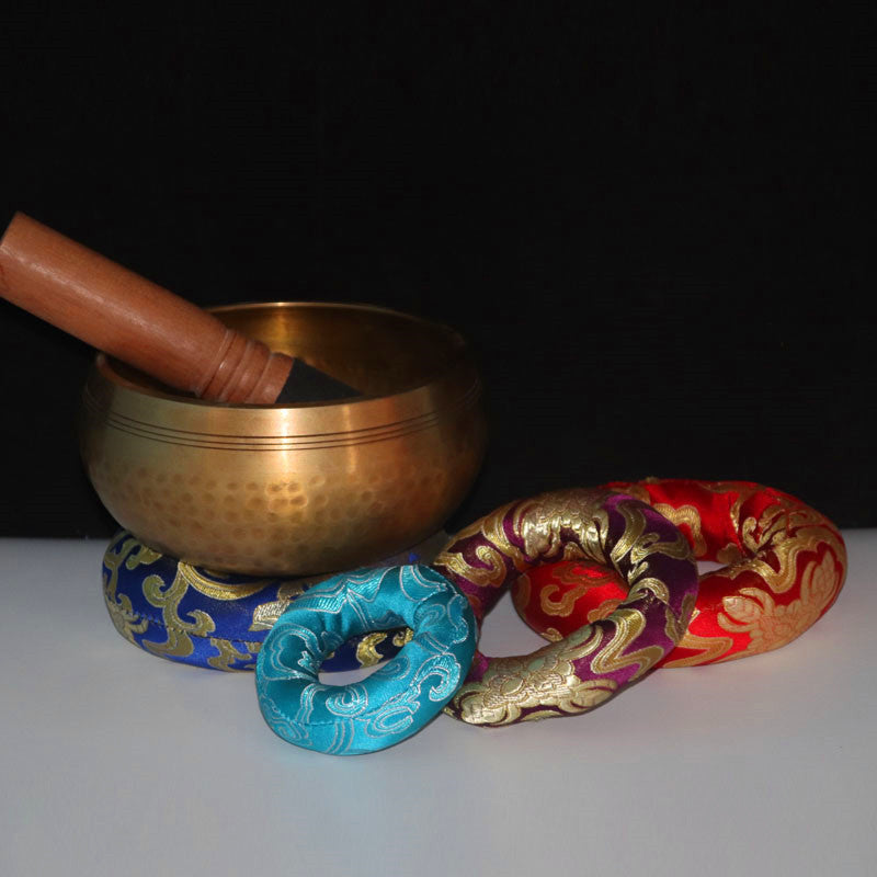 Bronze singing bowl with a mallet on a white surface with colorful cloths.