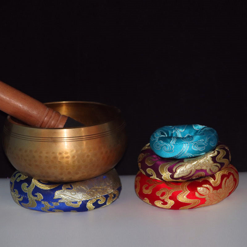 Brass singing bowl with a wooden mallet on a decorative stand against a black background