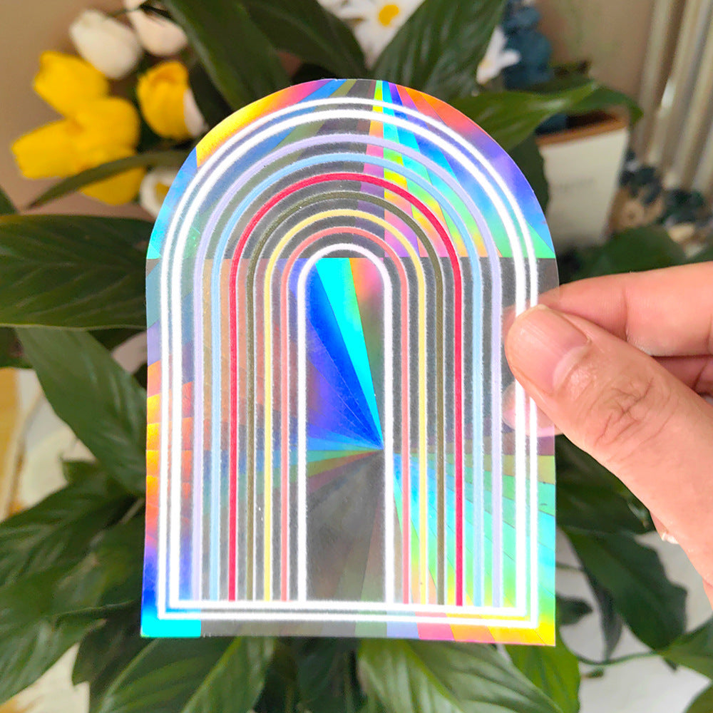 Holographic rainbow arch sticker held by a hand with plants in the background