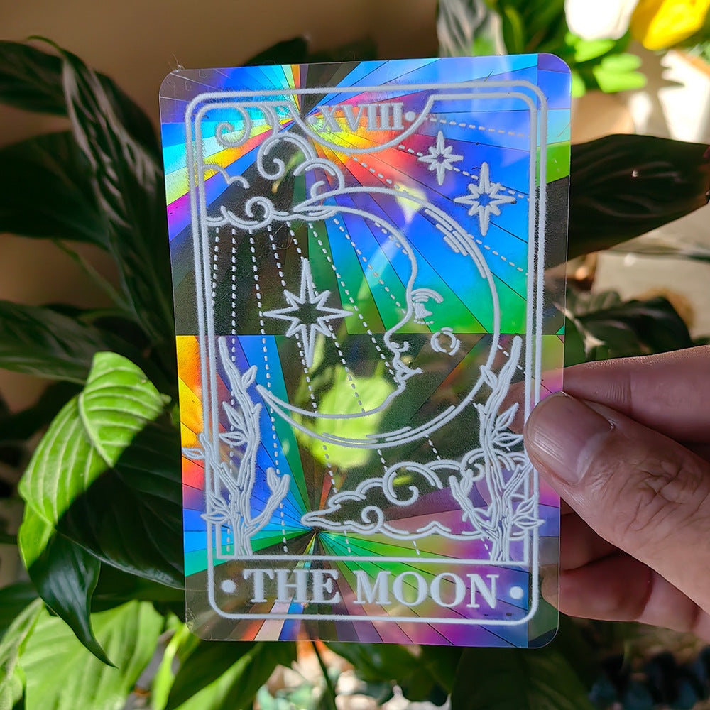 Holographic card with 'The Moon' design held in front of green leaves