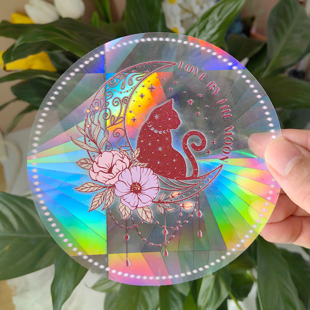 Holographic disc with cat and moon design held by a hand against a green leafy background