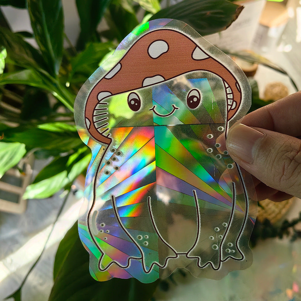 Holographic mushroom-shaped sticker held by a hand with green leaves in the background