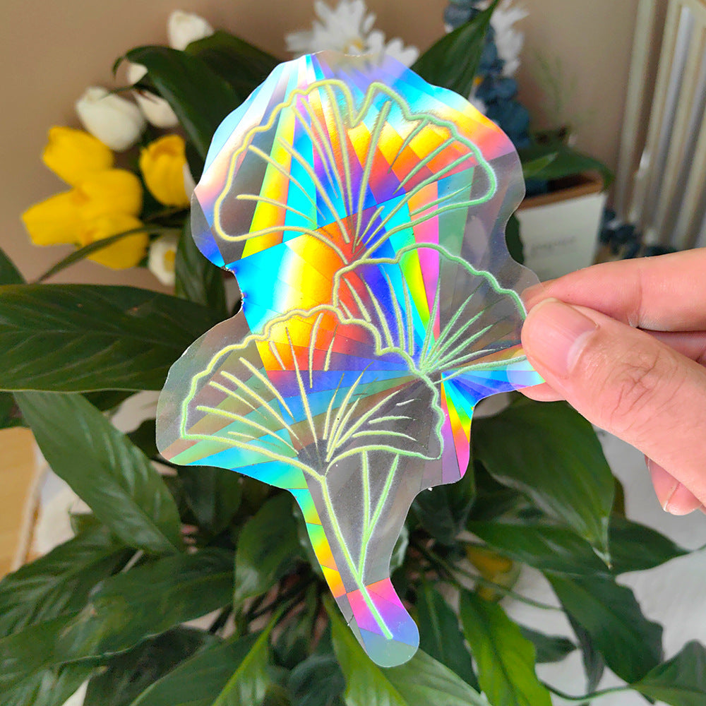 Holographic leaf-shaped sticker held by a hand with flowers in the background