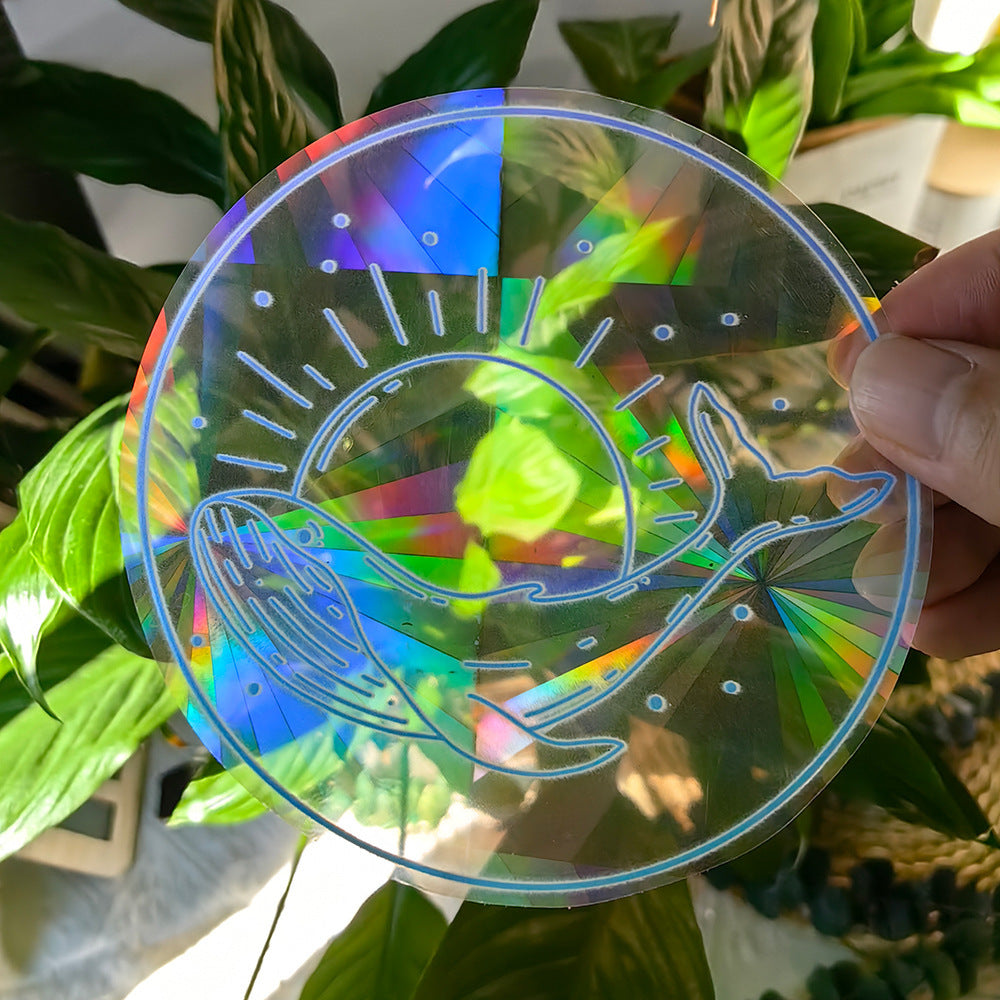 Holographic sun catcher with fish design held in front of green leaves
