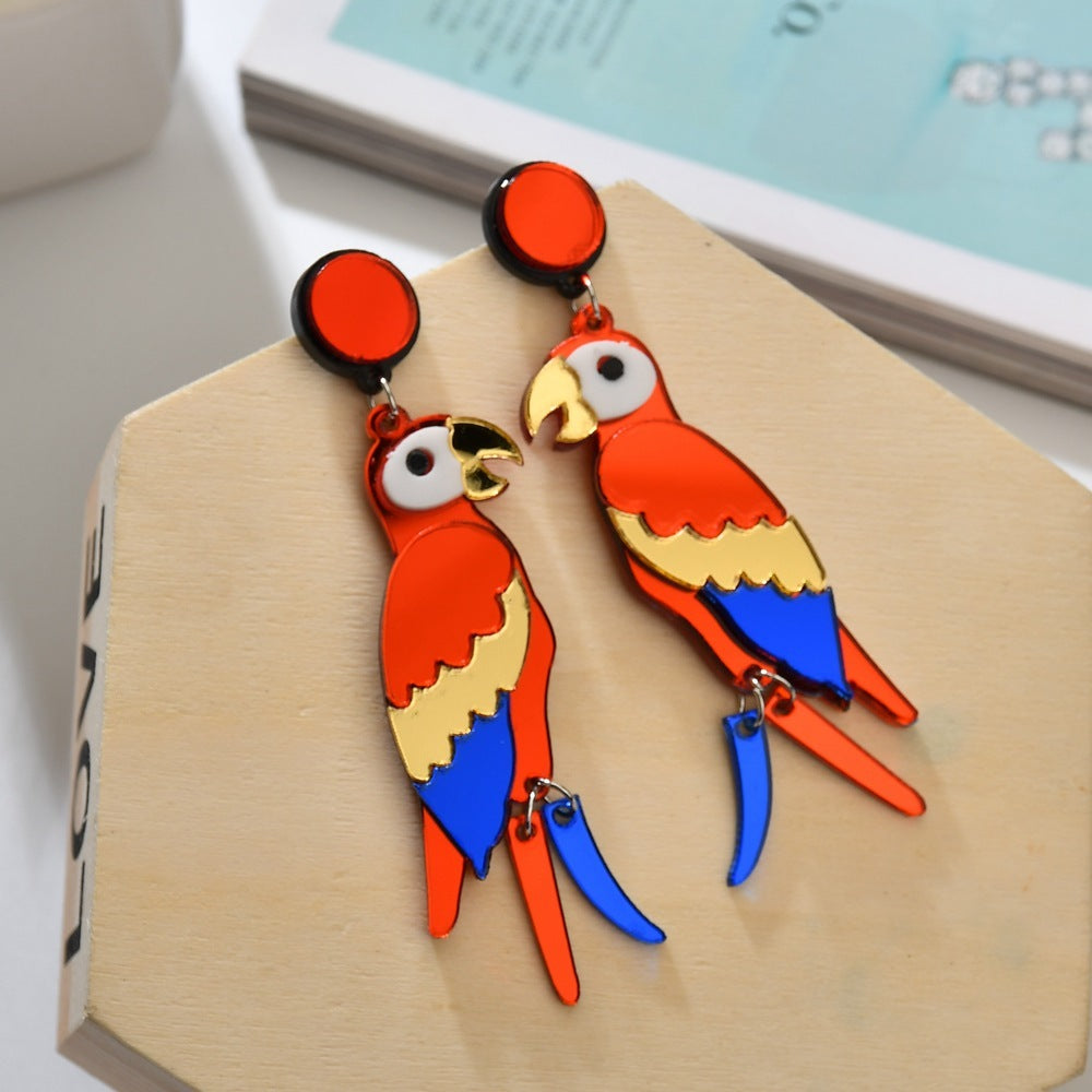 Colorful parrot-shaped earrings on a wooden block with a book in the background