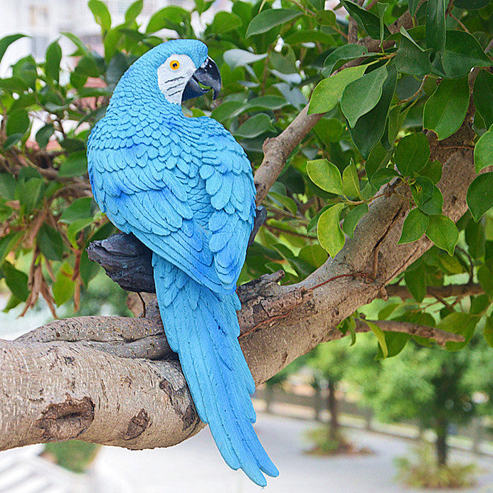 Blue parrot figurine on a branch with green leaves in the background