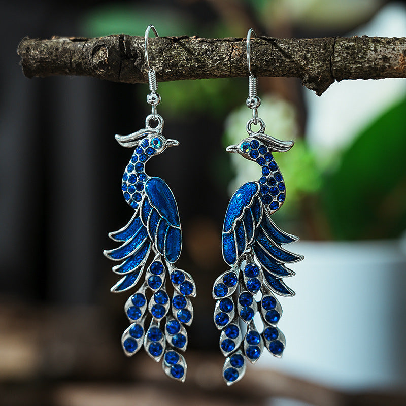 Blue peacock feather earrings hanging on a branch with a blurred natural background