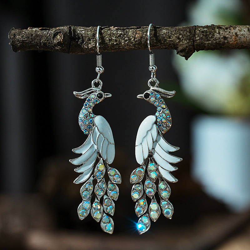 Pair of bird-shaped earrings with gemstones hanging on a branch.