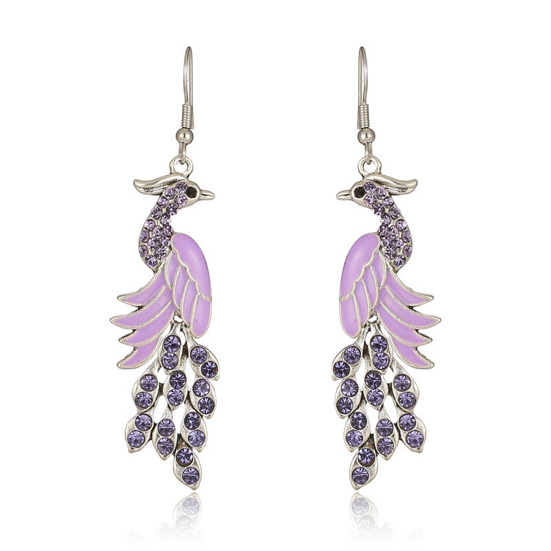 Purple peacock feather earrings with silver hooks on a white background