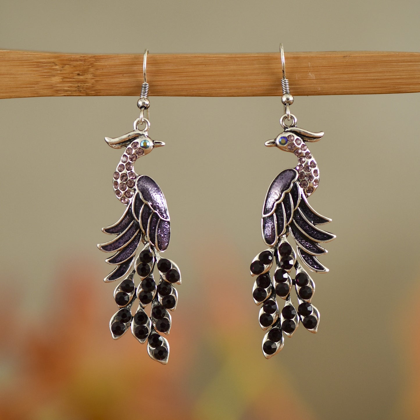 Pair of peacock-shaped earrings on a wooden stick with a blurred background