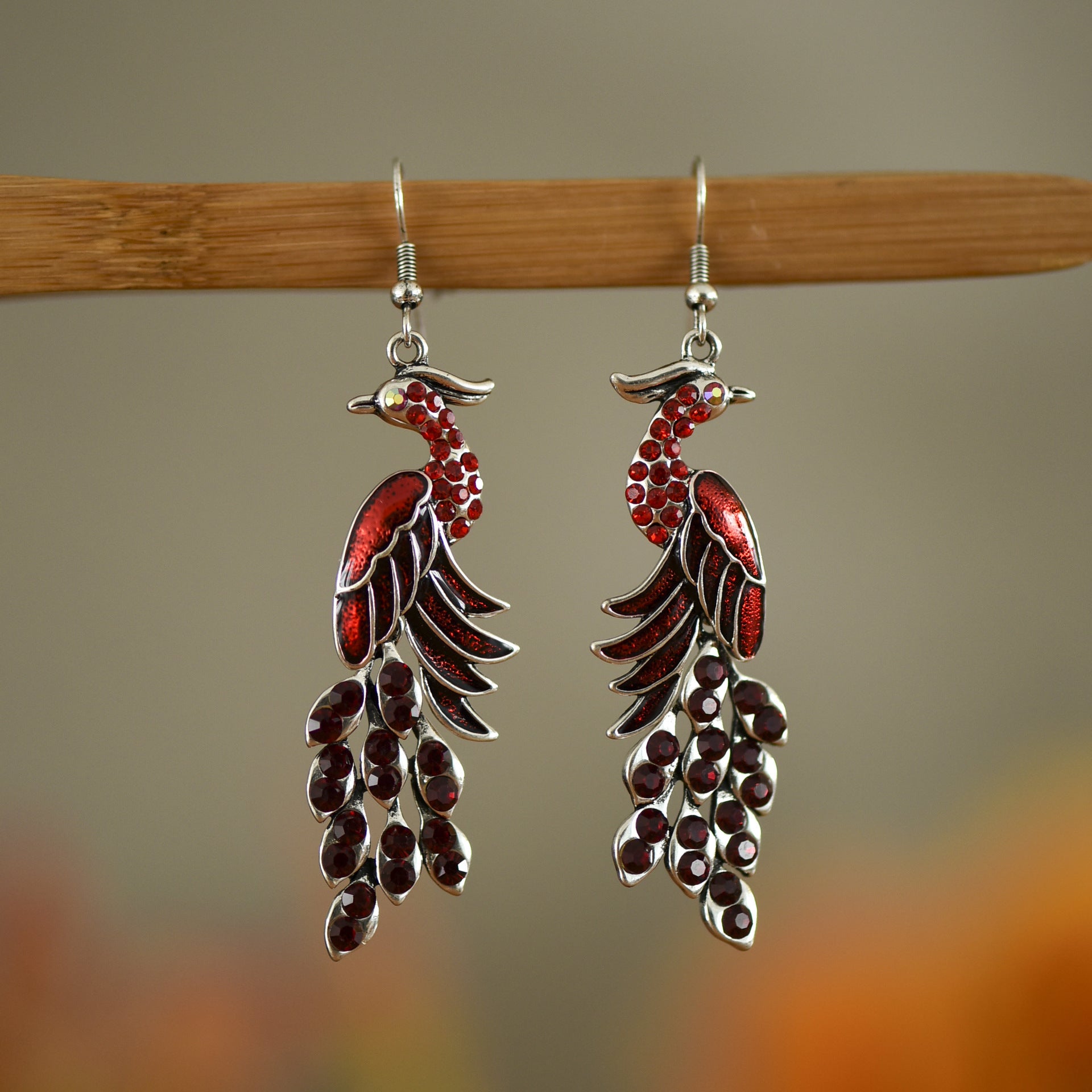 Red and silver feather-shaped earrings on a wooden stick with a blurred background
