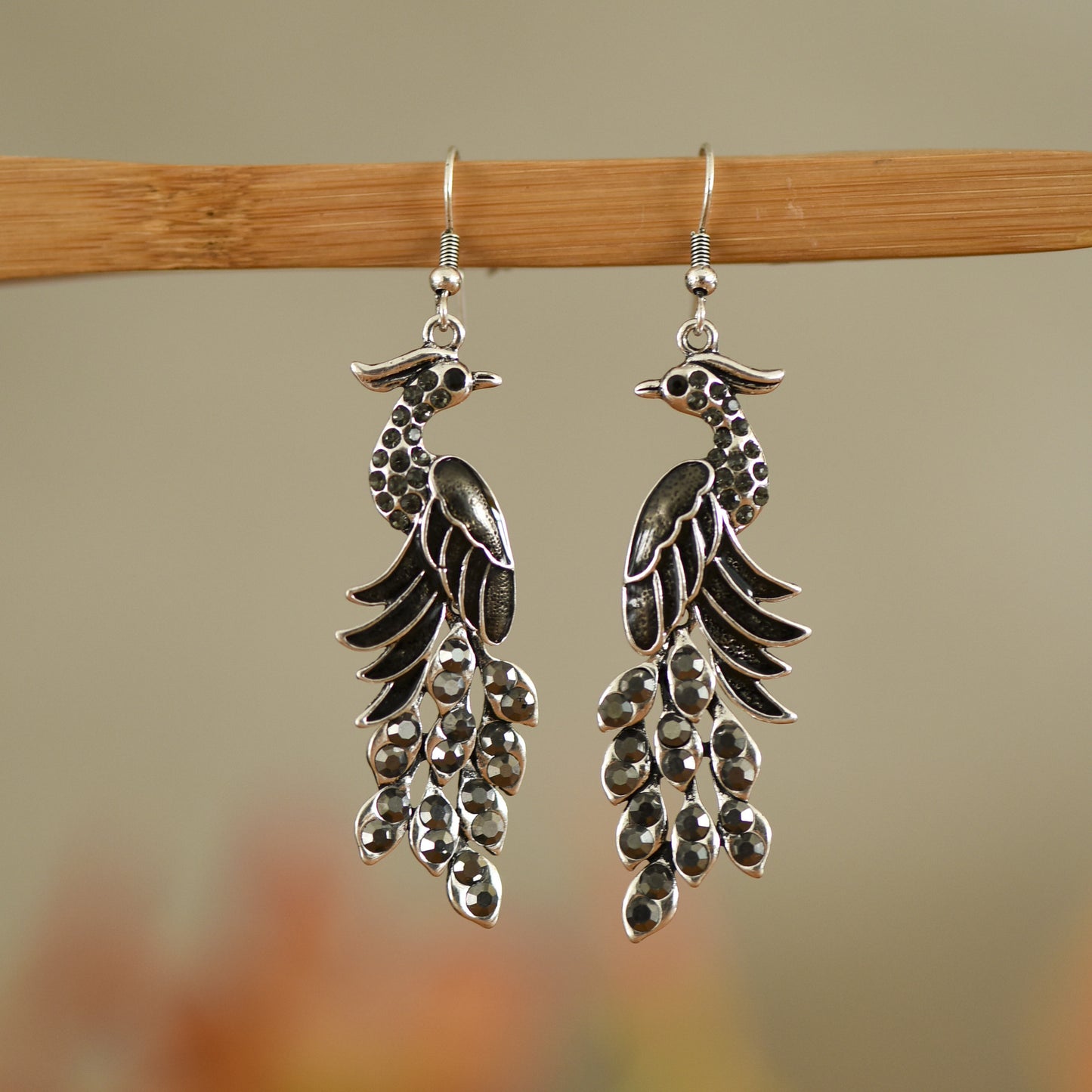 Silver peacock feather earrings on a wooden stick with a blurred background