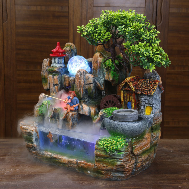 Decorative fountain with a small house, tree, and lantern on a wooden surface.