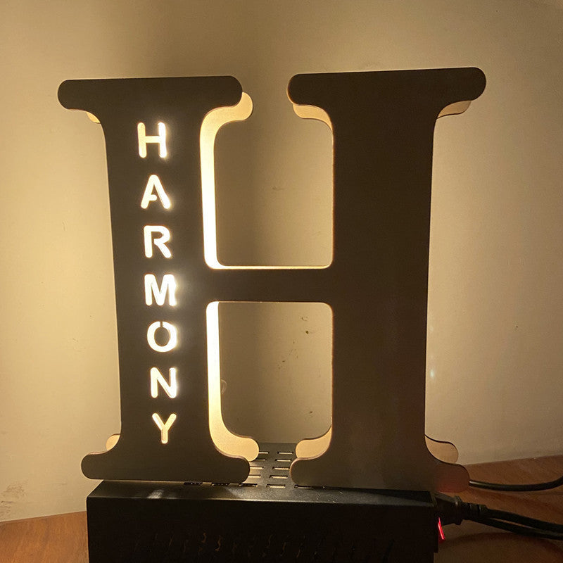 Decorative lamp shaped like the letter 'H' with 'HARMONY' illuminated inside, on a neutral background.