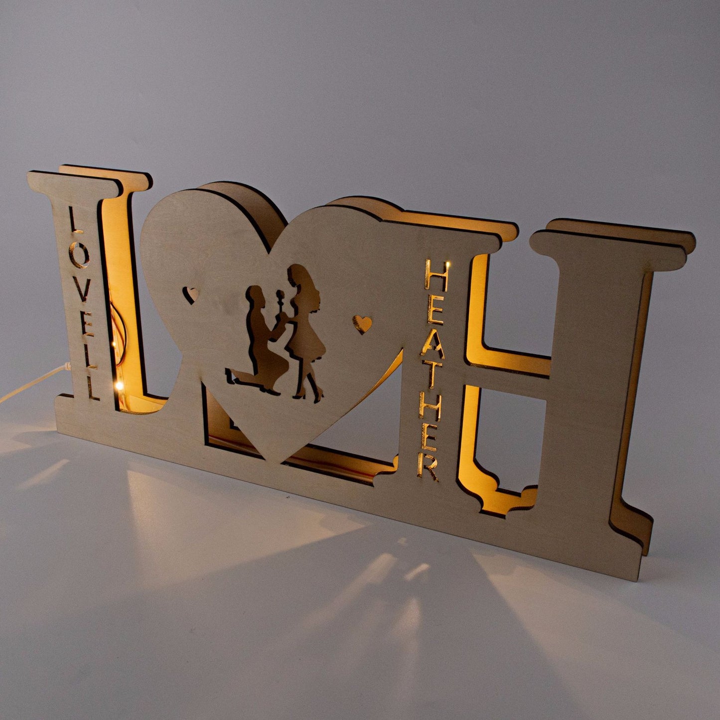 Wooden decorative sign with 'I ❤️ H' design, featuring cut-out figures and engraved names.