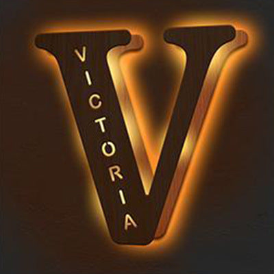 Wooden letter 'V' with 'VICTORIA' engraved on it, illuminated from behind.