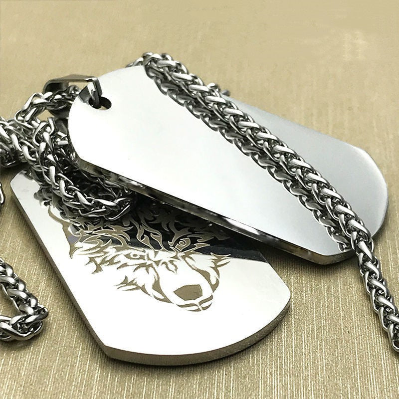 Two silver dog tags with a wolf engraving on a beige background