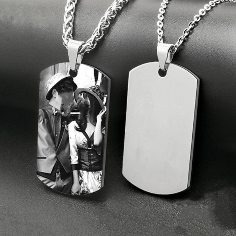 Two silver dog tag necklaces, one with a photo of a couple and the other plain, on a dark surface.
