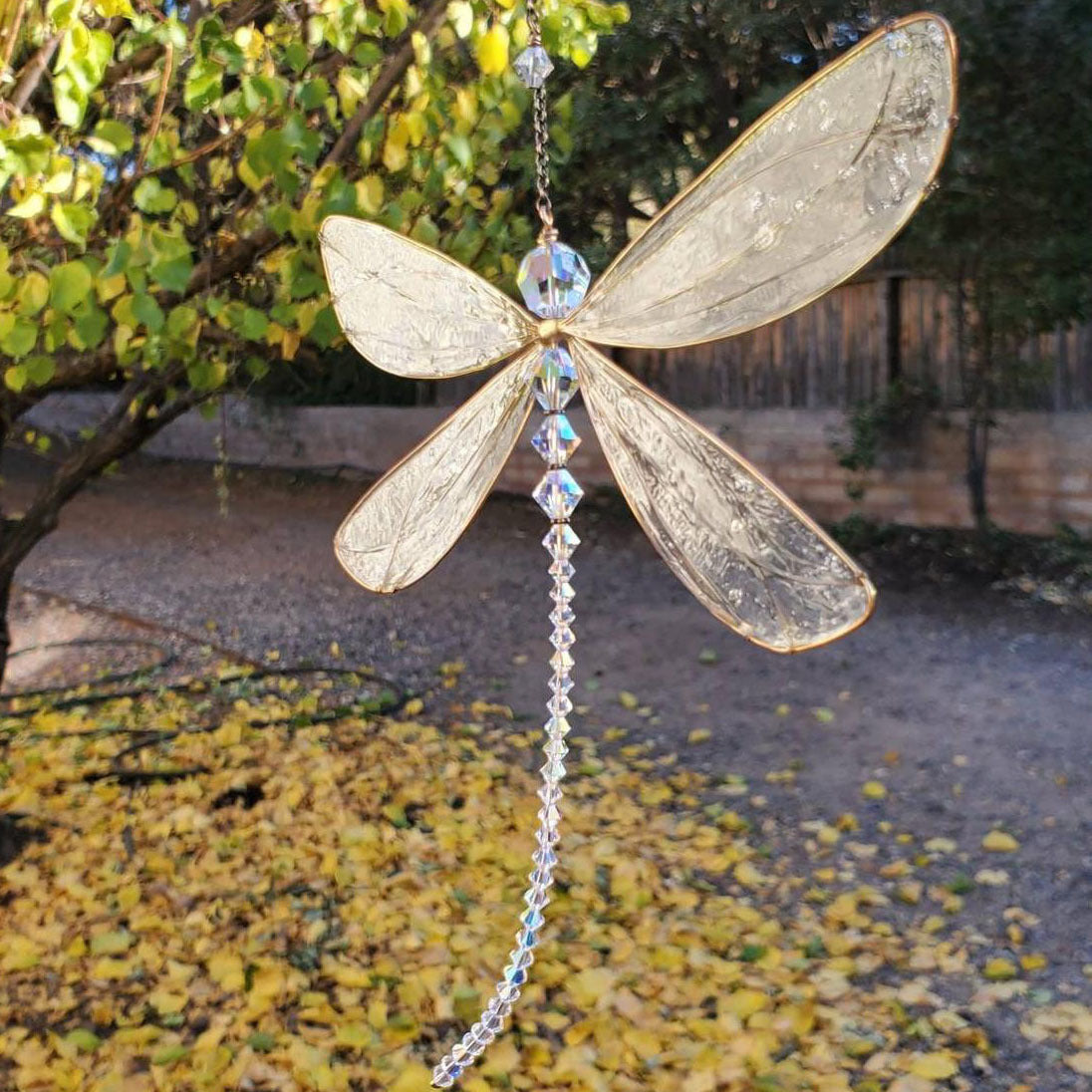 Decorative dragonfly ornament with crystals hanging outdoors.