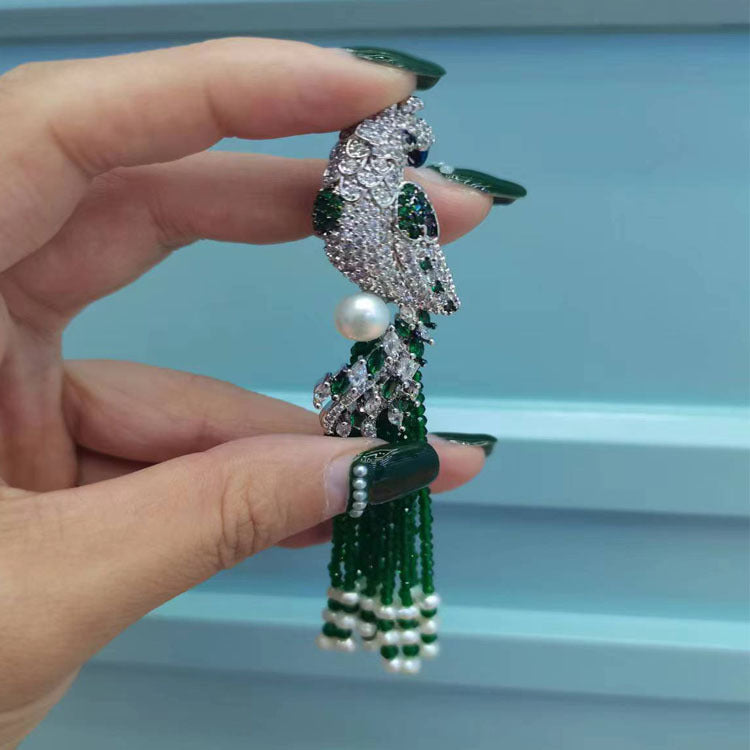 Hand holding a decorative green and silver brooch with pearls against a light blue background