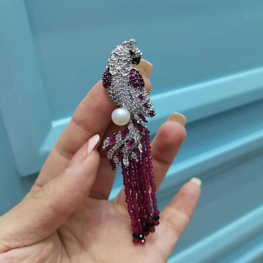 Hand holding a decorative parrot brooch with beads against a light blue background