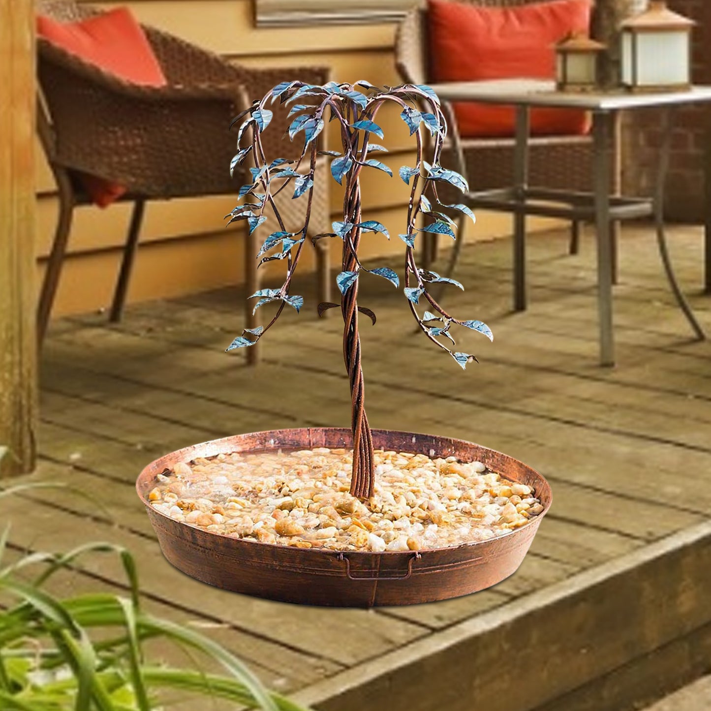Decorative metal tree in a bowl on a wooden deck with outdoor furniture in the background