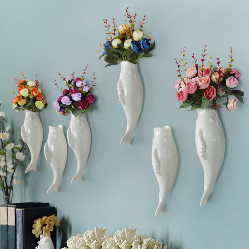 Decorative wall vases shaped like fish with floral arrangements on a light blue wall.