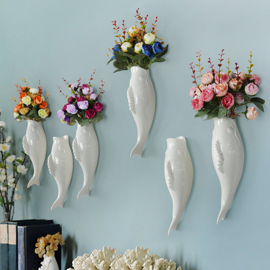 Decorative wall vases shaped like fish with floral arrangements on a light blue wall.