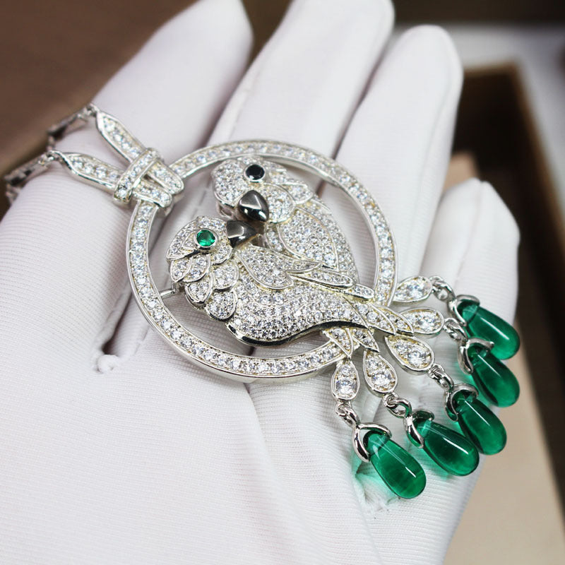 Delicate silver brooch with green gemstones held by a gloved hand.