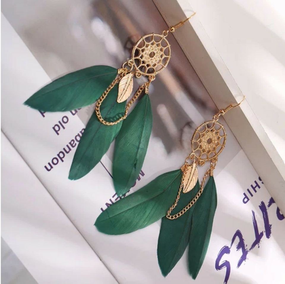 Gold earrings with green leaves on a magazine background