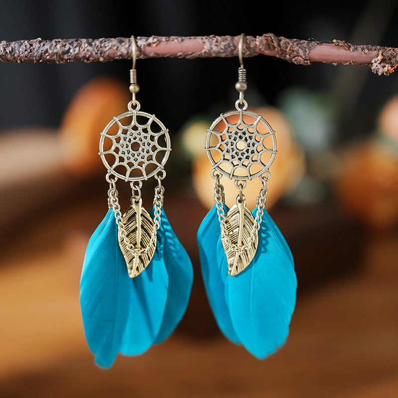 Pair of dreamcatcher earrings with blue feathers on a branch against a blurred natural background