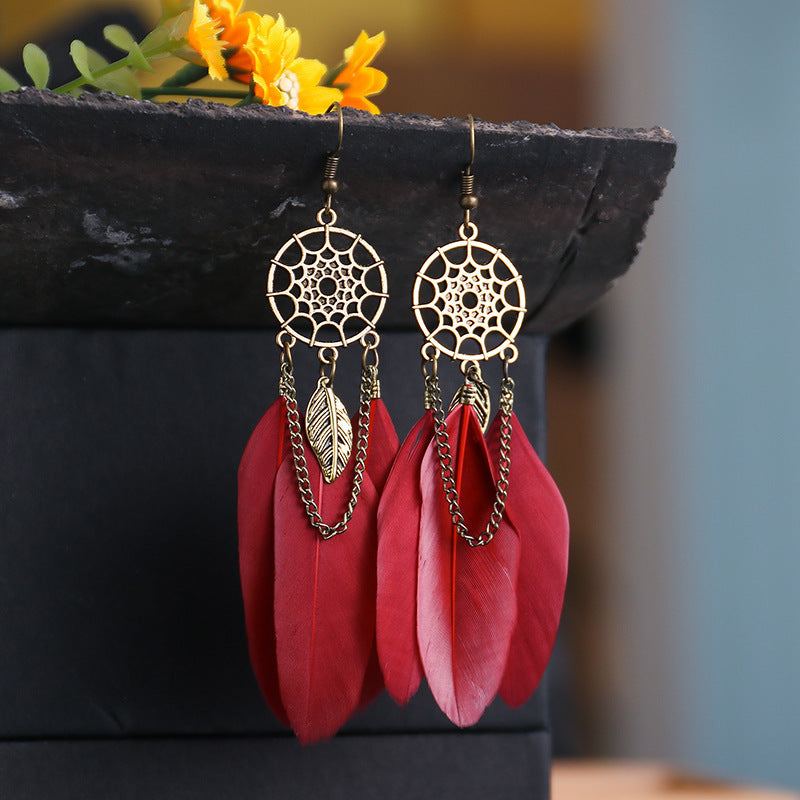 Gold and red feather earrings on a dark surface with flowers in the background
