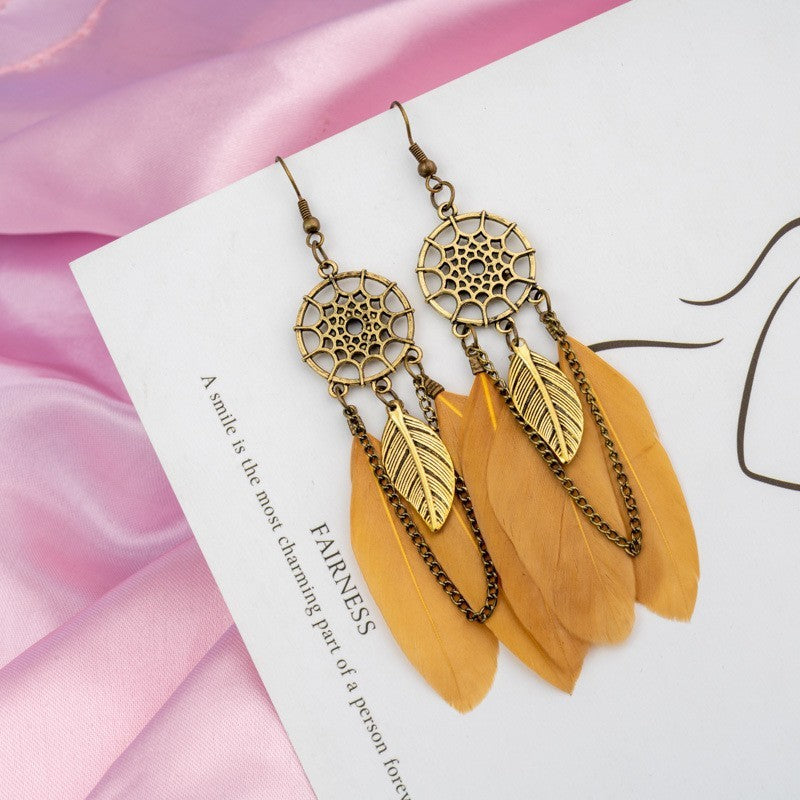 Gold and bronze dreamcatcher earrings with feathers on a pink fabric background