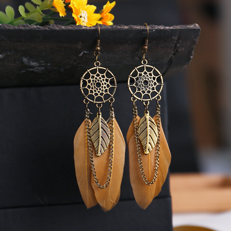 Gold dreamcatcher earrings with feathers on a dark surface with blurred background