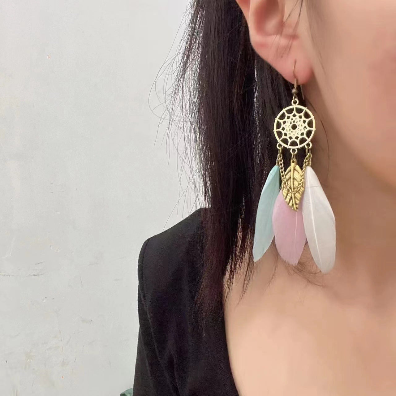 Earring with gold dreamcatcher design and colorful feathers on a plain background