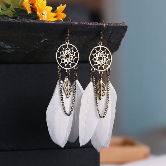 Gold dreamcatcher earrings with white feathers on a dark surface.