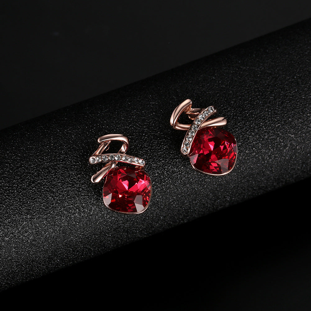 Pair of earrings with red gemstones and rose gold accents on a black background