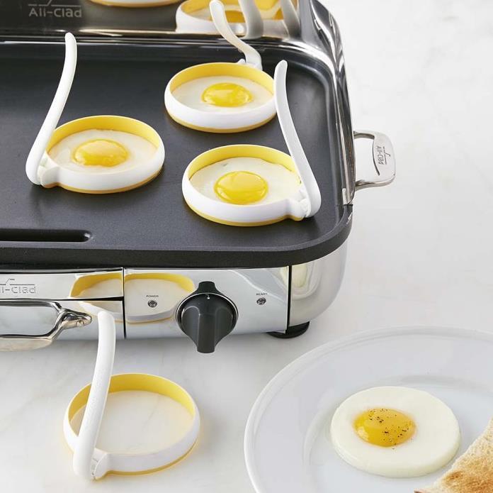 Egg cooking rings on a griddle with eggs being cooked, next to a plate with a cooked egg.