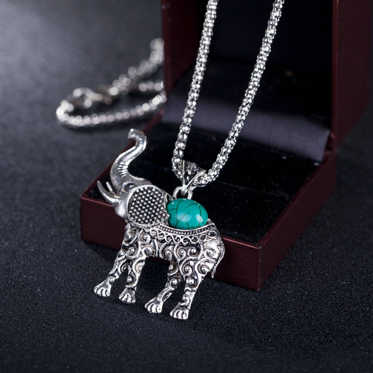 Silver elephant pendant necklace with turquoise gemstone on a dark background